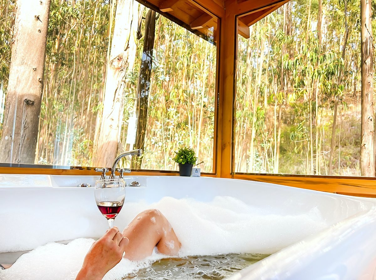Jacuzzi privado con espuma y una copa de vino dentro de un domo geodésico, con el bosque de eucaliptos a través del ventanal, en Pesca, Boyacá