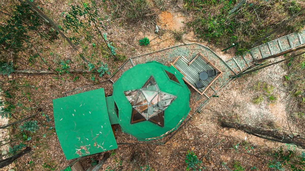 Vista cenital con dron de un domo geodésico y su terraza rodeados de bosque, en Pesca, Boyacá